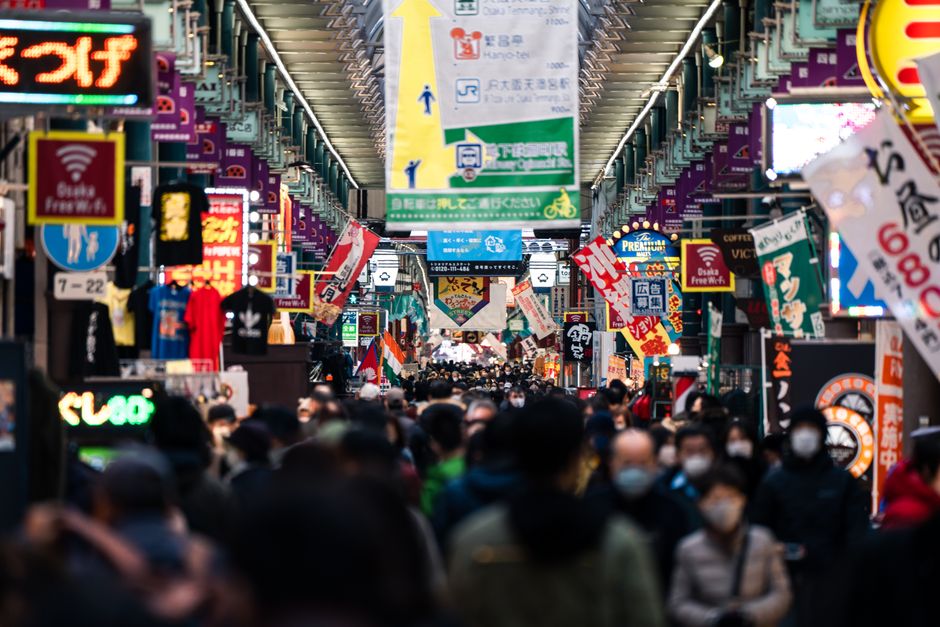 오사카 신사이바시 또는 우메다의 현대적인 쇼핑 거리. 사람들이 거닐고 명품 상점과 밝은 간판들이 도시적인 쇼핑 분위기를 연출한다.
