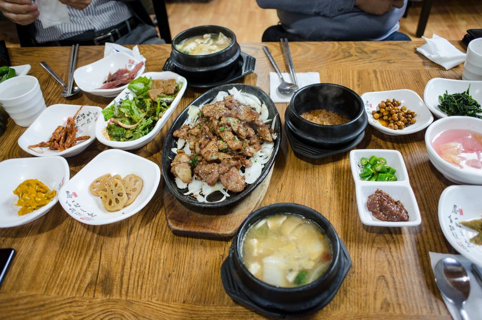 전주 한옥마을의 활기찬 길거리에서 맛볼 수 있는 다양한 먹거리들, 문꼬치, 닭날개볶음밥, 교동고로케 등이 먹음직스럽게 놓여있는 모습.